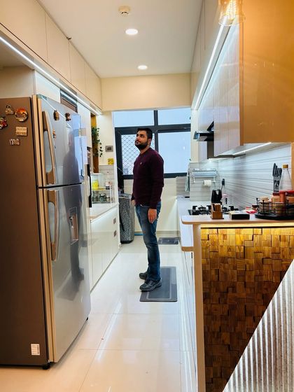 A full view of a completed modular kitchen at Nirala Estate. The design includes a double-door refrigerator, ample counter space, and a combination of wooden and white finishes for a warm, modern aesthetic.