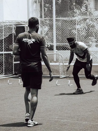 A coach observes an athlete performing hurdle drills. This black-and-white shot captures the focus and dedication present in our training sessions, where every movement is analyzed for improvement.