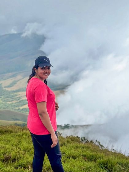 A smiling trekker posing against the cloud-covered peaks of Kudremukha.