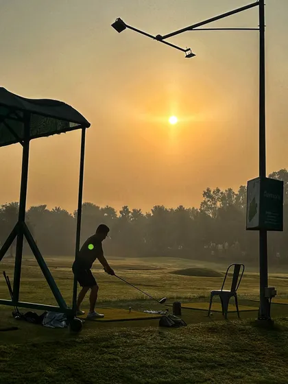 A golfer practices from a mat under the canopy, silhouetted against the rising sun.