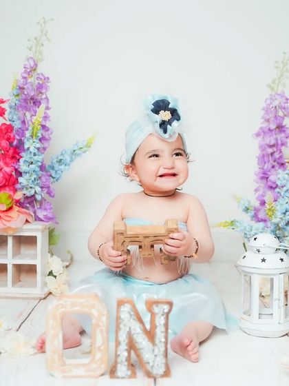 A happy baby girl surrounded by colorful flowers during her first birthday shoot.