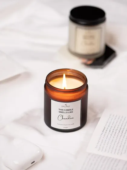 A warm and inviting shot of a lit candle, styled in a cozy, bed-time setting. The focus on the flame creates a sense of calm and relaxation.