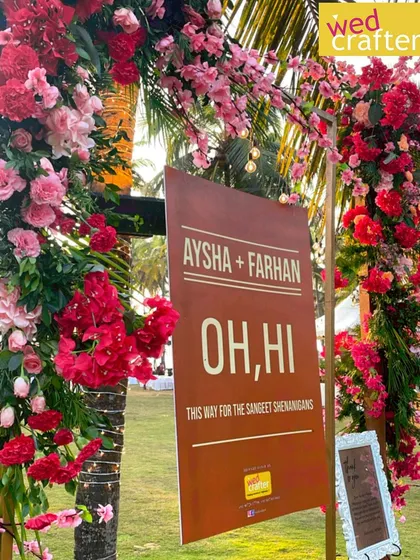 A fun and quirky welcome sign for the Sangeet, framed by an arch of vibrant pink flowers, setting a playful tone for the event.