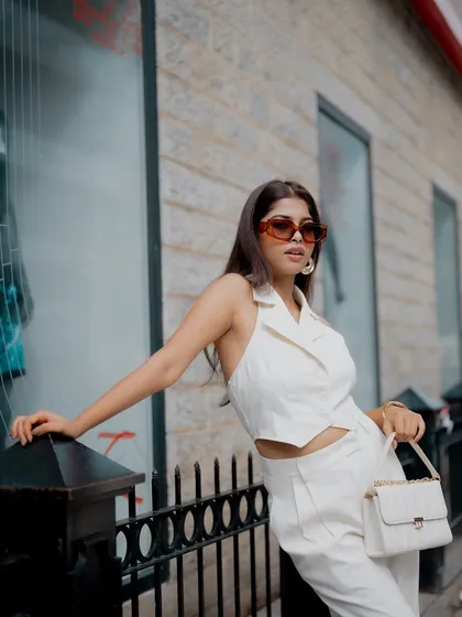 A stylish portrait of a model in an all-white outfit, leaning against a fence. The urban setting and her chic look create a sophisticated fashion image.