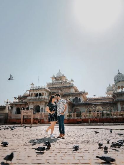 A wide shot showing the couple against the magnificent facade of Albert Hall Museum. The bright sun and scattered pigeons create a classic, cinematic feel for this Jaipur pre-wedding shoot.