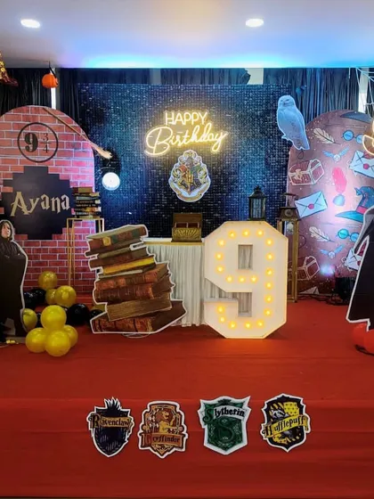 An immersive Harry Potter themed stage decoration for a 9th birthday. The setup includes a Platform 9 3/4 backdrop, a shimmer wall, character cutouts, and props like a stack of books.