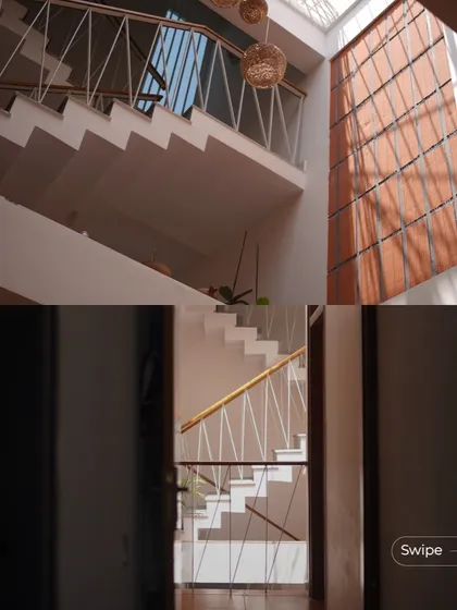 The elegant white staircase of the Gopal Residence, with its delicate railing, stands in contrast to the warm terracotta wall, all illuminated by a large skylight.