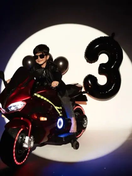 A cool and confident three-year-old poses on his toy motorcycle against a spotlight. This is a great example of a themed shoot for an older child.