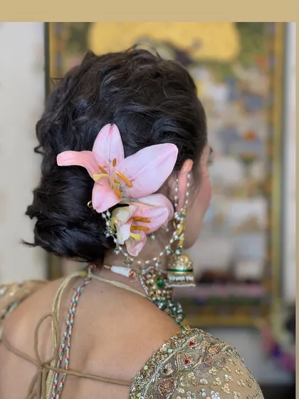 A beautiful messy bun accented with fresh pink lilies. Using larger flowers like these creates a bold and artistic statement, perfect for a daytime wedding or mehendi.