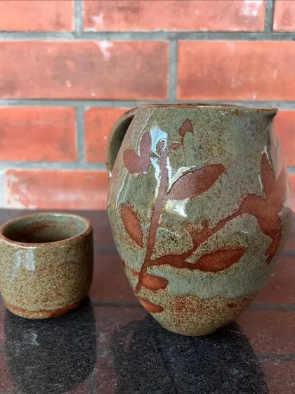 A rustic pitcher and cup set with a warm, earthy glaze and leaf-like wax-resist patterns.