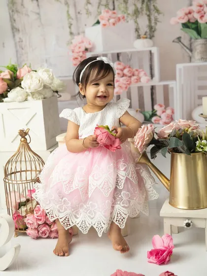 A bright, happy smile from the birthday girl, holding a pink peony. The floral props are interactive and safe for babies, adding another layer of fun to the shoot.