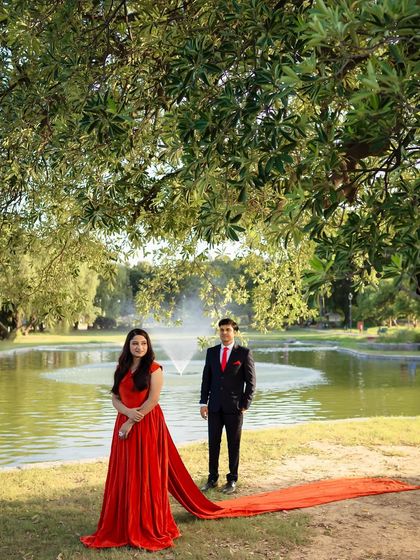 This orange-red crepe gown features a stylish overlap design and a manageable trail. It's a chic and modern choice for a pre-wedding shoot in a park or garden setting.