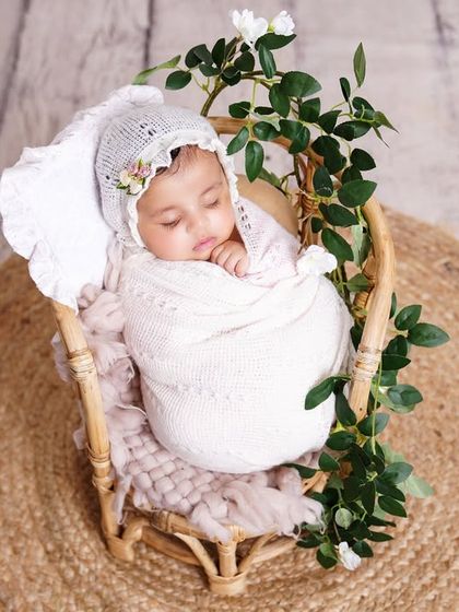 An overhead shot of a newborn sleeping peacefully in a rustic basket, swaddled in white and surrounded by delicate greenery.