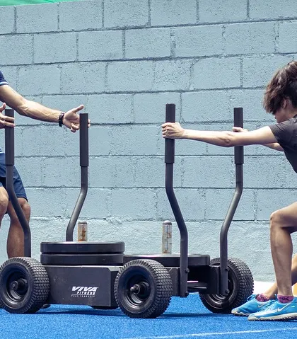 A coach assists an athlete with a sled push on our turf. This is a fantastic tool for developing horizontal force production and full-body power, directly translating to improved acceleration and speed.