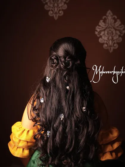 A romantic half-up hairstyle with rose-shaped buns and soft curls. This look, created for a mehendi, is playful yet elegant.