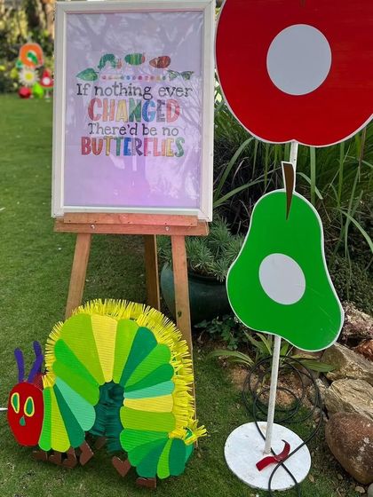 I created a complete scene from 'The Hungry Caterpillar', including the caterpillar himself and oversized cardboard cutouts of the pear and apple he eats. The framed quote adds a sweet, thematic touch to the party entrance.