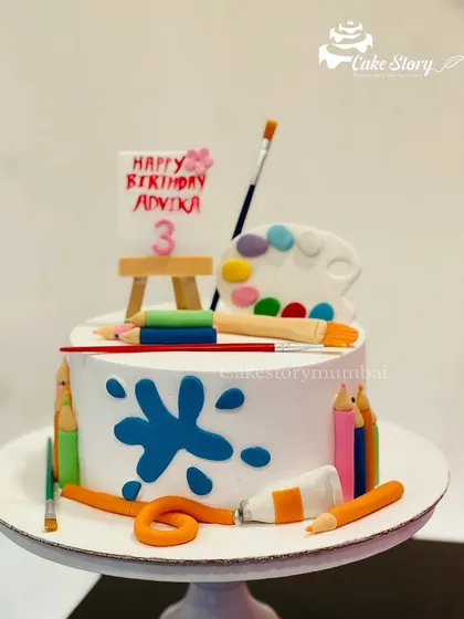 A cake for a little artist. This design is decorated with an edible easel, paint palette, brushes, and color pencils, all handcrafted from fondant.