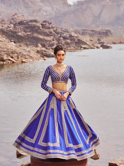 A regal blue lehenga with geometric gold embroidery. The structured A-line skirt and long-sleeved blouse create a powerful and elegant silhouette, perfect for an evening celebration.