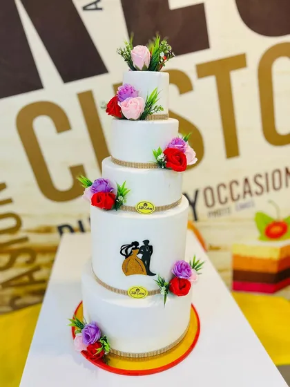 This grand 10kg, five-tiered wedding cake is a perfect example of classic elegance. Each tier is finished with smooth white fondant and decorated with delicate, colorful sugar flowers and a silhouette of a couple, showcasing our ability to create large, stunning cakes for your most important day.