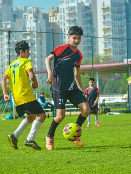 An intense one-on-one battle for the ball against the backdrop of Gurgaon's modern buildings.