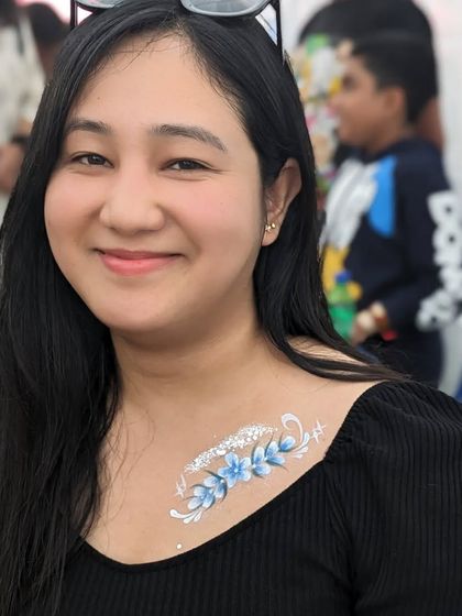 A delicate blue floral design on the collarbone, accented with silver glitter.