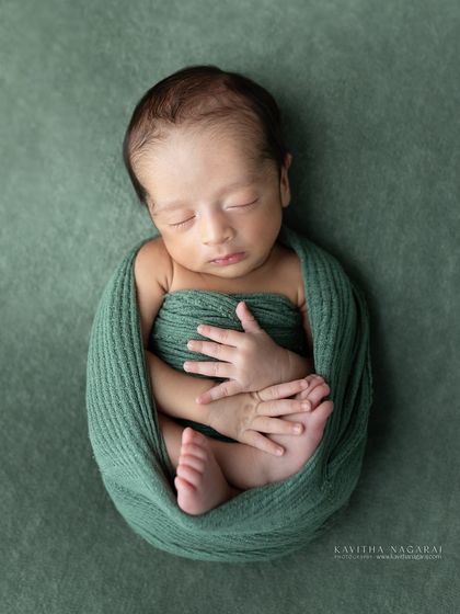 A one-week-old newborn named Aryan, wrapped snugly in a green swaddle. The simplicity of the pose highlights his delicate features and the freshness of his first days.