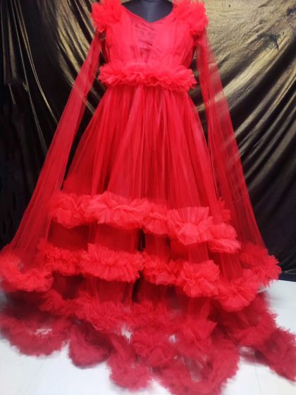 This dramatic red ball gown features a tiered, ruffled skirt and a sheer cape for an extra touch of elegance. It's a statement rental piece for any special occasion.