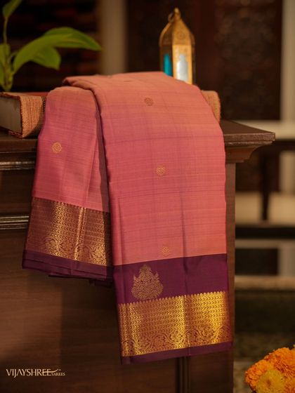 A stunning pink and violet Kanjivaram, its beauty enhanced by the warm lighting of our store. This piece features delicate gold buttas and a rich zari border.
