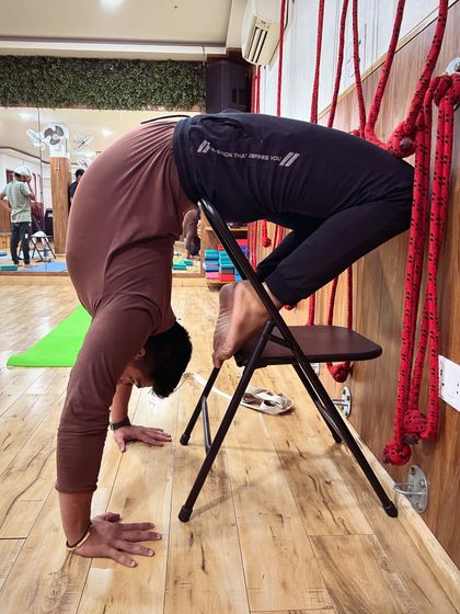 Another angle of the chair-supported backbend, this time incorporating the wall ropes for added stability. This setup allows for a safe and deep spinal extension.