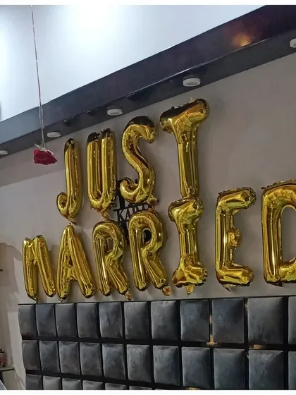A clear shot of the "Just Married" foil balloons in gold, placed prominently above the headboard. This is a simple but essential element for any honeymoon suite decoration.