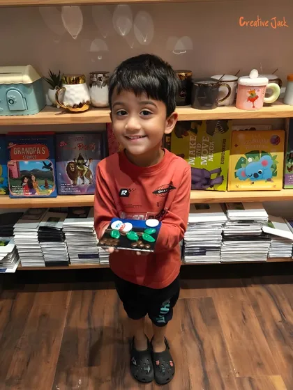 A smiling boy holds up his completed clay project. My workshops for kids focus on building confidence and providing a sense of accomplishment.