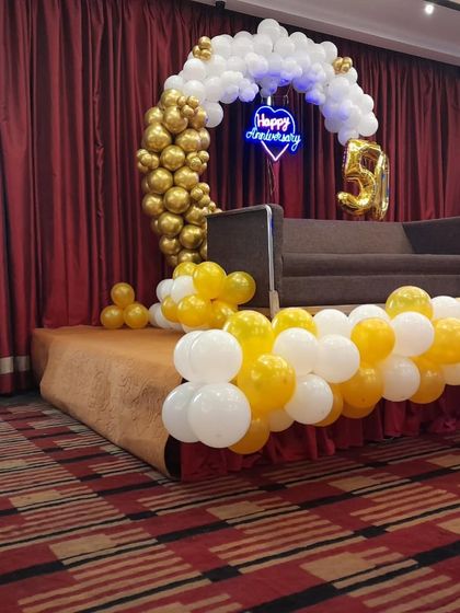 A side view of the anniversary stage, highlighting the half-arch design with a cascade of golden balloons on one side and white on the other.