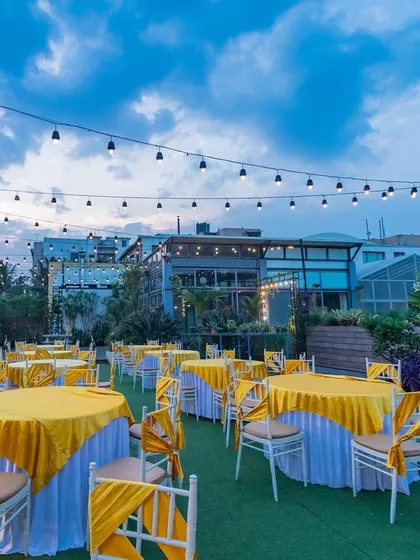 A daytime view of the Terrace Garden with yellow-themed dining tables set up under the open sky and string lights.