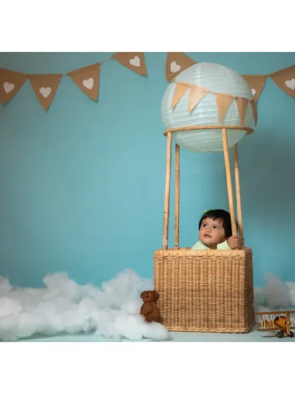 A curious baby looking out from the hot air balloon basket against a calm blue sky.