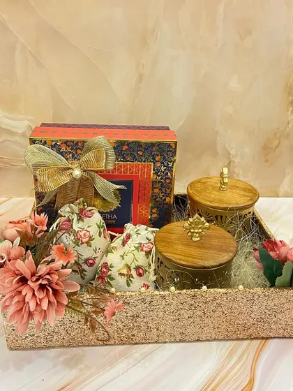 Our festive platters are perfect for any celebration. This glittery tray holds decorative jars, a mithai box, and floral potlis, all adorned with beautiful artificial flowers.