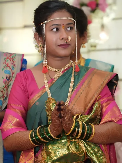 A portrait of the bride with her hands joined in prayer. This image highlights the green glass bangles, mehndi, and the traditional nath, all part of the complete bridal package.