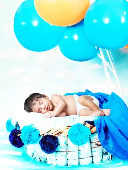 A creative 'hot air balloon' setup, with a sleeping baby in a basket lifted by blue and yellow balloons.