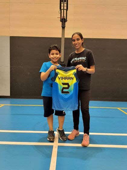 Officially welcoming Vihaan to the Maniac family! A coach and a new young player proudly hold up his personalized jersey.