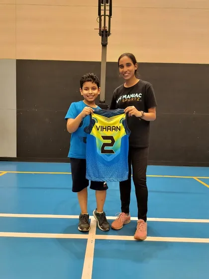 Officially welcoming Vihaan to the Maniac family! A coach and a new young player proudly hold up his personalized jersey.