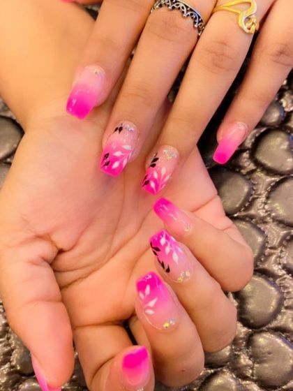 A beautiful pink ombre on coffin-shaped nails. The design is enhanced with hand-painted white and black leaves, creating a lovely floral effect over the gradient.