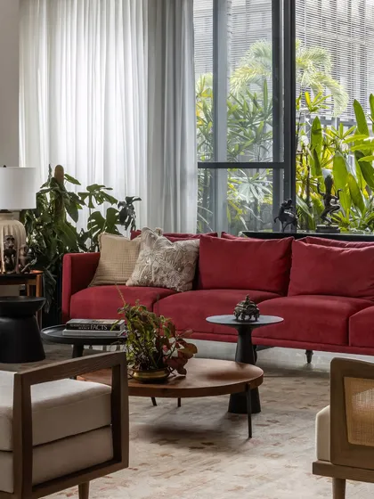 Another angle of the living room, showing the interplay of the red sofa against the backdrop of lush greenery seen through the large windows.