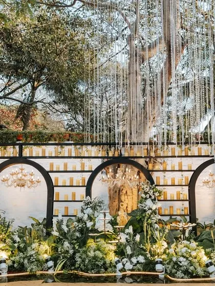 A closer look at the engagement stage, detailing the candle wall, the elegant chandeliers within the arches, and the lush bed of white and green florals at the base.