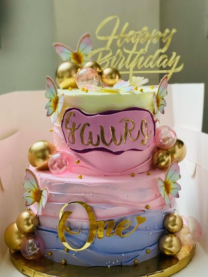 A magical two-tier cake for a first birthday, with pastel colors, butterflies, and gold accents.