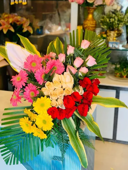 A large and impressive standing bouquet arrangement. It features a colorful mix of pink, yellow, and red gerberas and roses, perfect for congratulating someone on a big achievement.