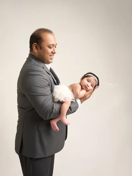 A father holds his newborn daughter carefully in his hands, a pose that beautifully illustrates just how tiny and delicate she is.
