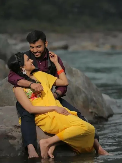 A relaxed and romantic photo of a couple sitting by the river, their feet dipped in the water.