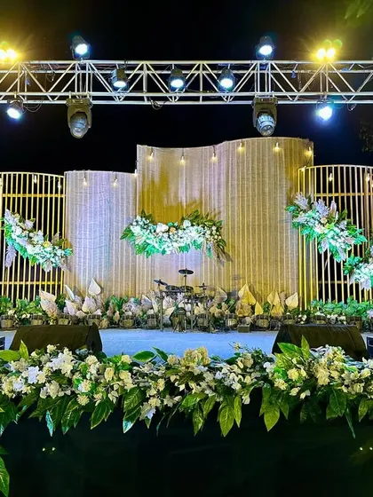 A boho-themed Sangeet stage, using natural textures like bamboo and pampas grass, combined with modern lighting and white florals.