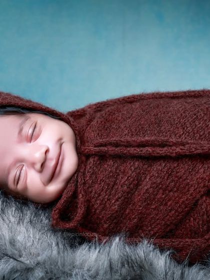 A sweet, smiling newborn wrapped in a deep brown swaddle, resting on a soft fur blanket. The rich, warm tones are perfect for creating a cozy atmosphere.