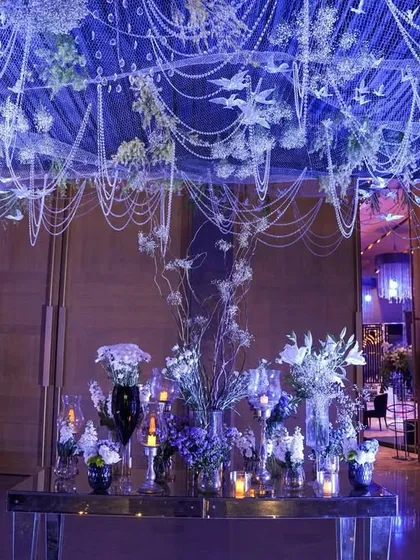 A magical entrance featuring a ceiling of cascading pearls and bird motifs, with a table of fresh white and purple florals creating a dreamy, whimsical welcome.