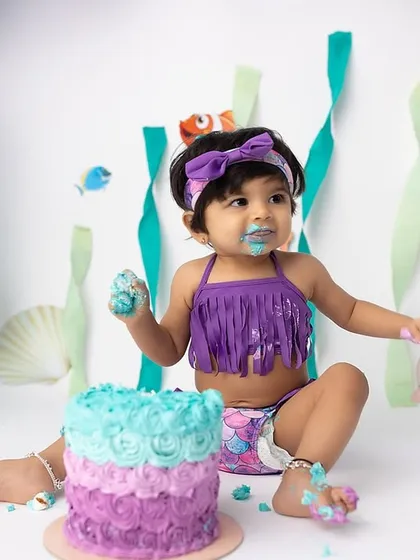 A perfect mermaid pose! This little girl is enjoying every moment of her first birthday cake smash, surrounded by balloons and under-the-sea decorations.